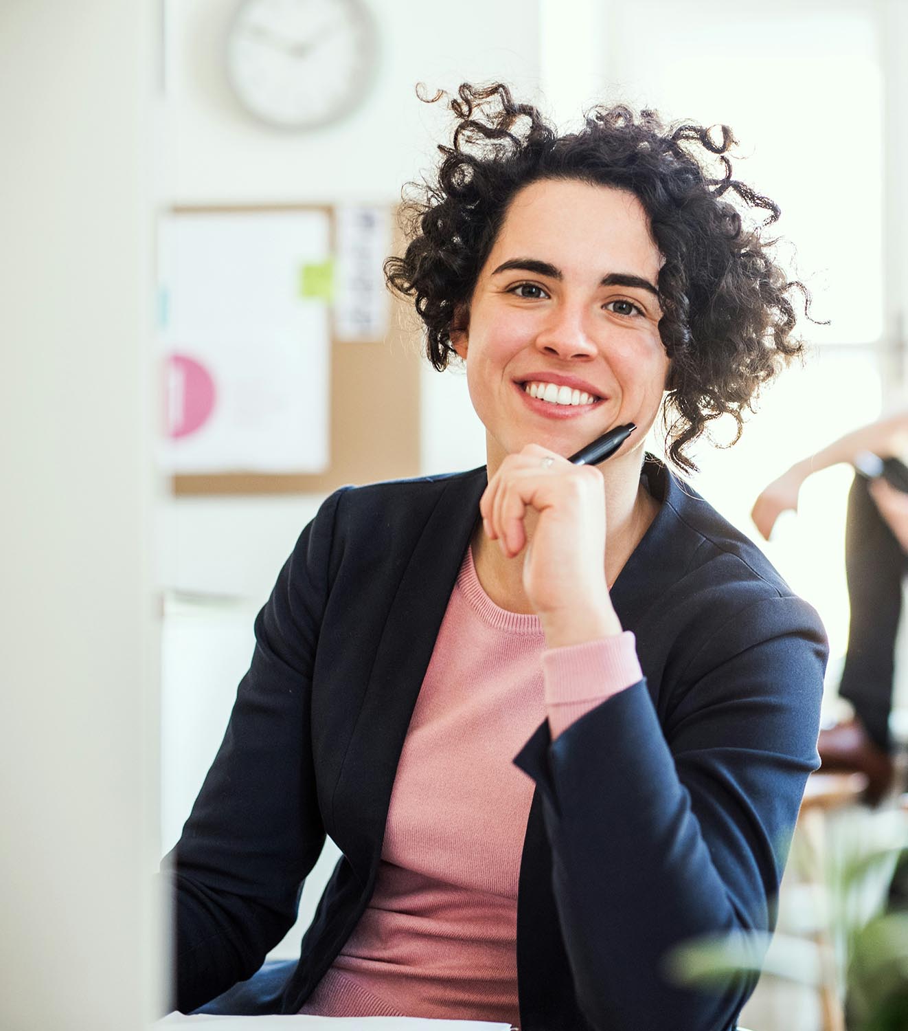 Fotografía de una mujer trabajando cómodamente con su ordenador en una oficina, con una sonrisa y mirando directamente a la cámara.