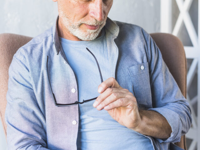 Hombre mayor sonriente sentado frente a un ordenador portátil en un entorno luminoso.